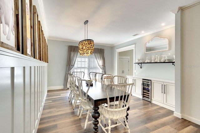 dining space featuring wine cooler, crown molding, wood-type flooring, and an inviting chandelier