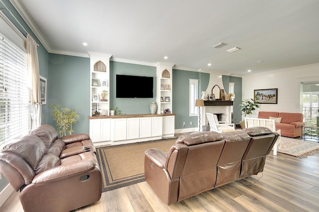 living room with crown molding, a brick fireplace, light hardwood / wood-style flooring, and built in features