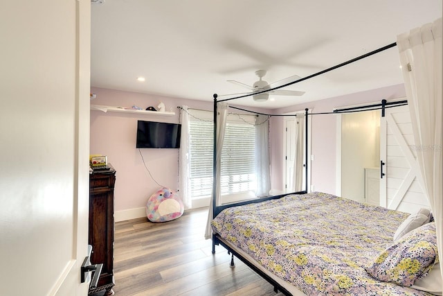 bedroom featuring a barn door, ceiling fan, and light wood-type flooring