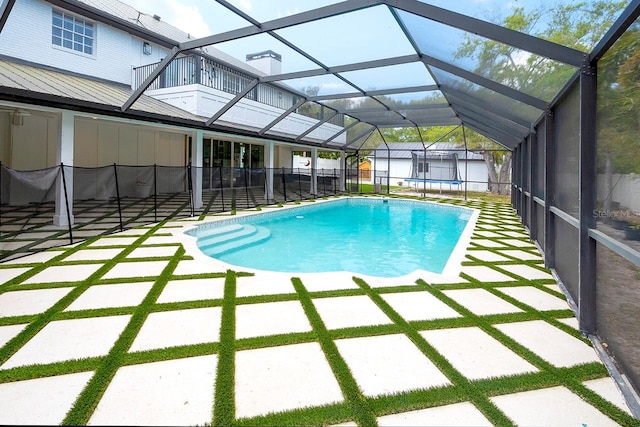 view of swimming pool featuring glass enclosure, a storage unit, and a patio area