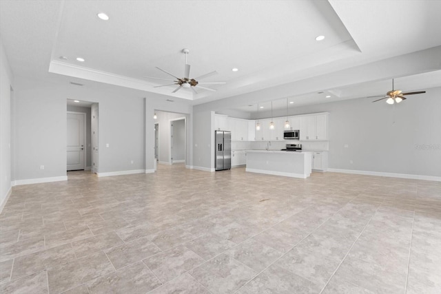 unfurnished living room featuring ceiling fan, sink, and a tray ceiling