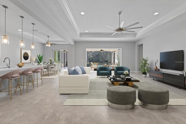 living room featuring a textured ceiling, a raised ceiling, ornamental molding, and sink