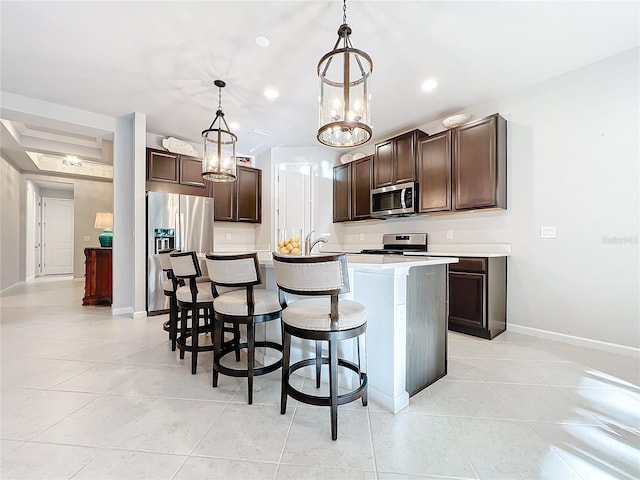 kitchen featuring a breakfast bar, dark brown cabinets, stainless steel appliances, hanging light fixtures, and an island with sink