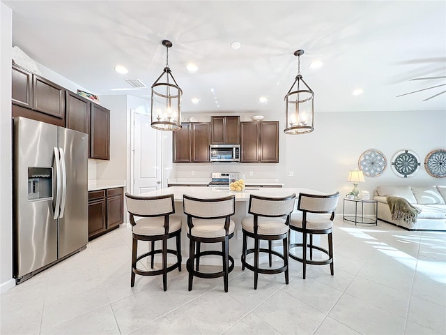 kitchen featuring a kitchen bar, dark brown cabinets, stainless steel appliances, pendant lighting, and a center island