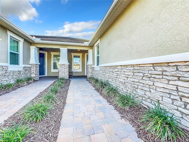 view of exterior entry with stucco siding, stone siding, and covered porch