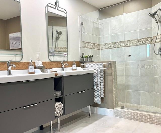 bathroom with tile flooring, tiled shower, and dual vanity