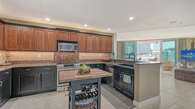 kitchen with light tile flooring, stainless steel appliances, sink, tasteful backsplash, and dark stone countertops