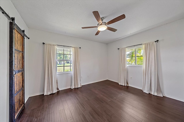 unfurnished room with a barn door, dark hardwood / wood-style flooring, ceiling fan, and a wealth of natural light