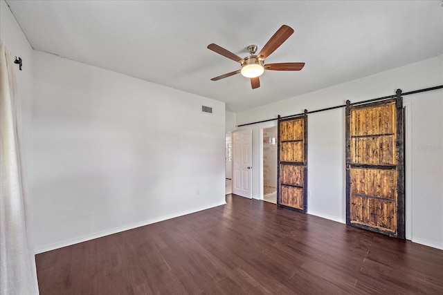 empty room with a barn door, dark hardwood / wood-style flooring, and ceiling fan