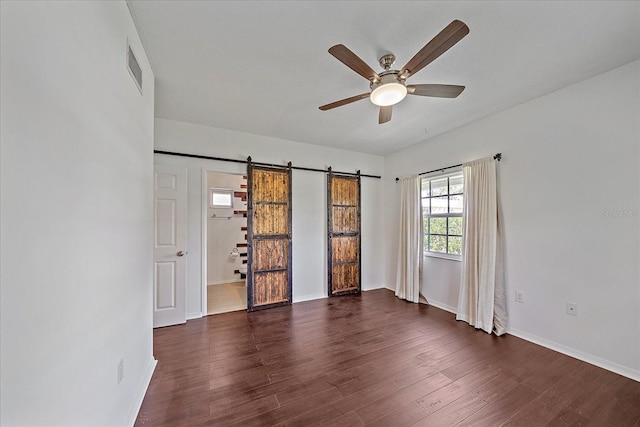 spare room with a barn door, ceiling fan, and dark hardwood / wood-style flooring