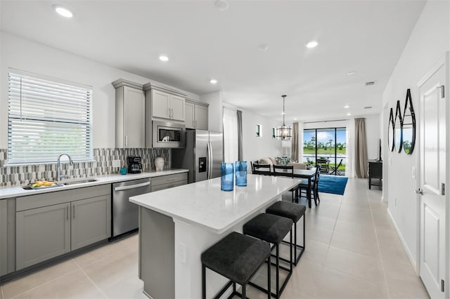 kitchen featuring a kitchen island, light tile flooring, tasteful backsplash, appliances with stainless steel finishes, and gray cabinetry