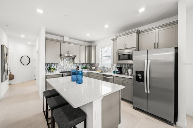 kitchen with stainless steel appliances, a kitchen island, light tile floors, a kitchen breakfast bar, and backsplash