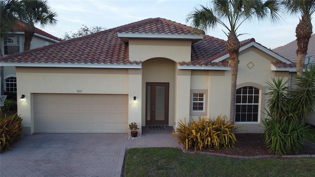 mediterranean / spanish home with a garage, decorative driveway, a tile roof, and stucco siding