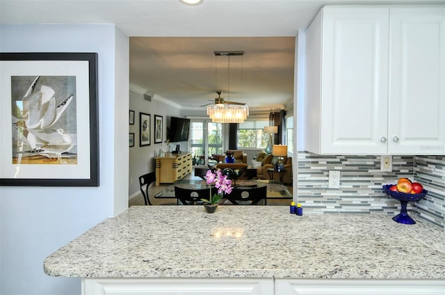 kitchen with hanging light fixtures, backsplash, white cabinets, light stone counters, and ornamental molding