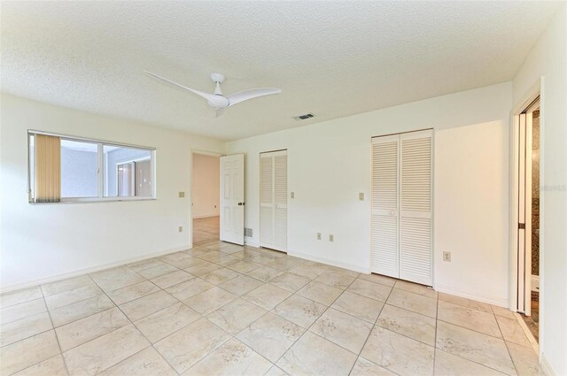 unfurnished bedroom featuring ceiling fan, light tile patterned floors, a textured ceiling, and two closets