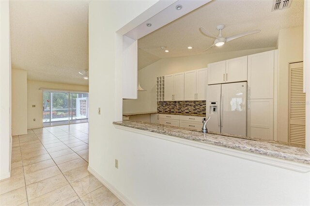 kitchen featuring light stone counters, light tile flooring, white fridge with ice dispenser, backsplash, and ceiling fan