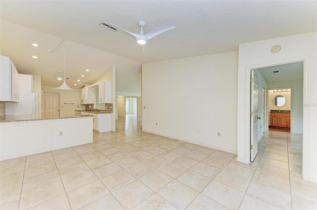 unfurnished living room featuring ceiling fan, vaulted ceiling, a textured ceiling, and light tile floors