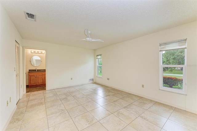 tiled empty room with a wealth of natural light, sink, ceiling fan, and a textured ceiling