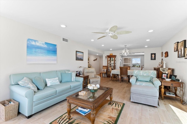 living room featuring ceiling fan with notable chandelier and light wood-type flooring