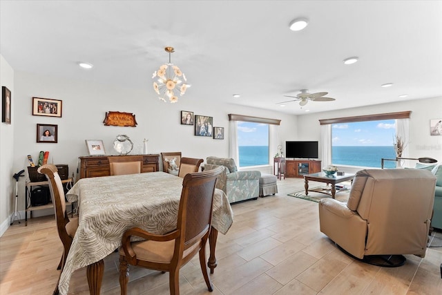 dining room with a water view, light wood-type flooring, and ceiling fan with notable chandelier