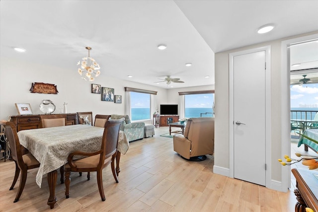 dining room with light hardwood / wood-style floors, ceiling fan with notable chandelier, a water view, and a wealth of natural light