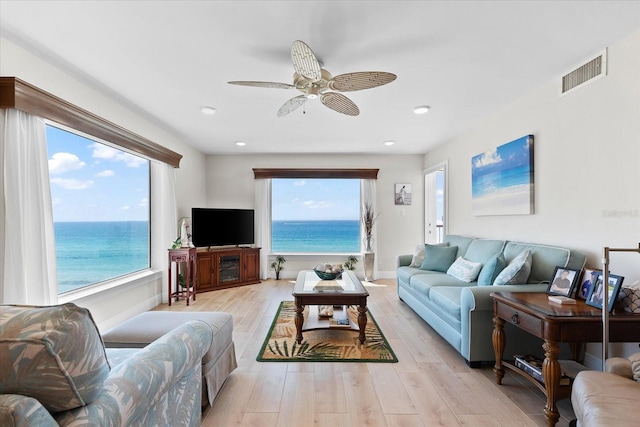 living room featuring a healthy amount of sunlight, light hardwood / wood-style floors, ceiling fan, and a water view