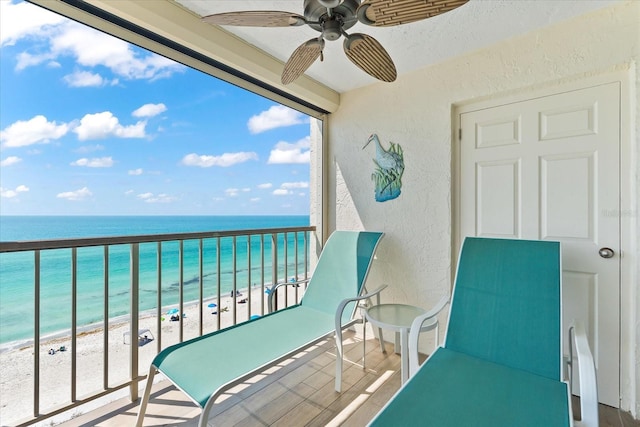 balcony featuring a view of the beach, ceiling fan, and a water view