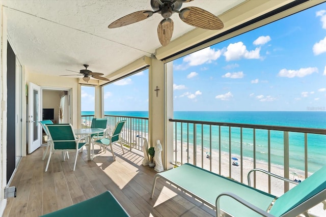 balcony with a beach view, ceiling fan, and a water view