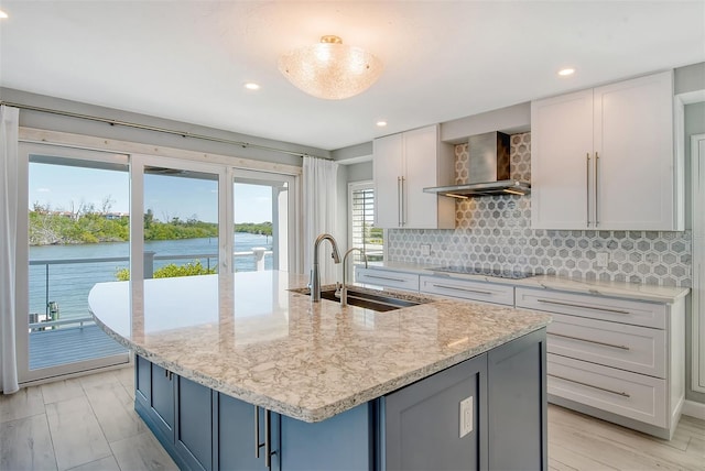 kitchen featuring white cabinets, light stone countertops, wall chimney range hood, sink, and tasteful backsplash