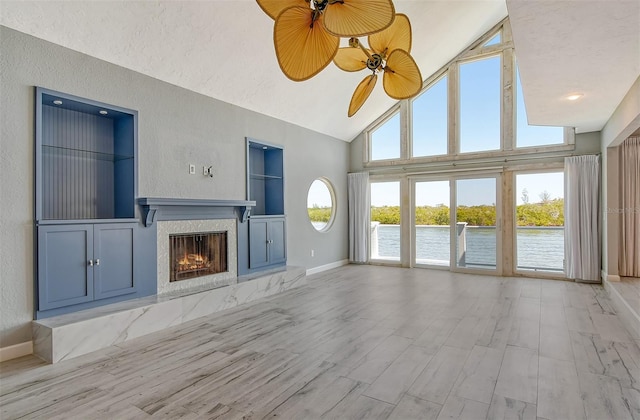 unfurnished living room with ceiling fan, a premium fireplace, high vaulted ceiling, light hardwood / wood-style floors, and plenty of natural light