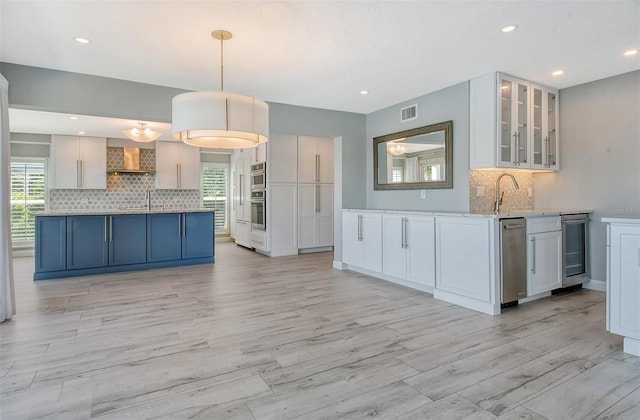 kitchen with wall chimney exhaust hood, decorative light fixtures, and white cabinetry