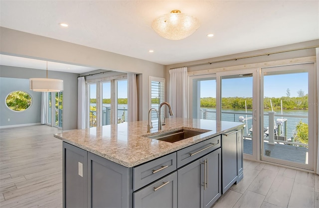 kitchen featuring light stone counters, a water view, sink, decorative light fixtures, and light hardwood / wood-style flooring