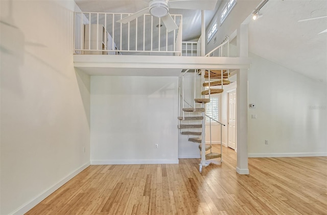 interior space with rail lighting, a towering ceiling, ceiling fan, and light wood-type flooring