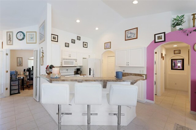 kitchen featuring white cabinets, a kitchen bar, light tile flooring, and white appliances