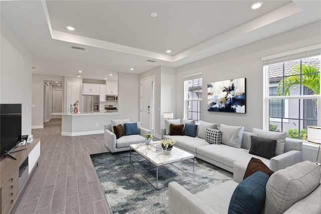 living room with light hardwood / wood-style floors, a healthy amount of sunlight, and a tray ceiling