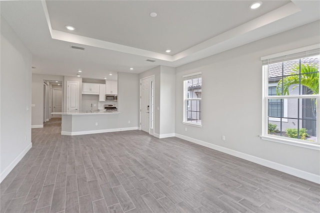 unfurnished living room with a raised ceiling, light hardwood / wood-style floors, and a wealth of natural light