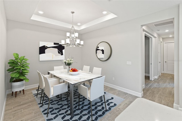 dining space featuring a tray ceiling, light hardwood / wood-style floors, and an inviting chandelier