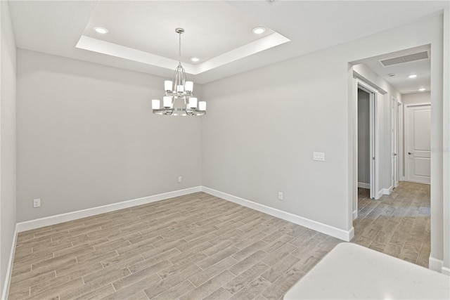 empty room with a raised ceiling, an inviting chandelier, and light hardwood / wood-style floors