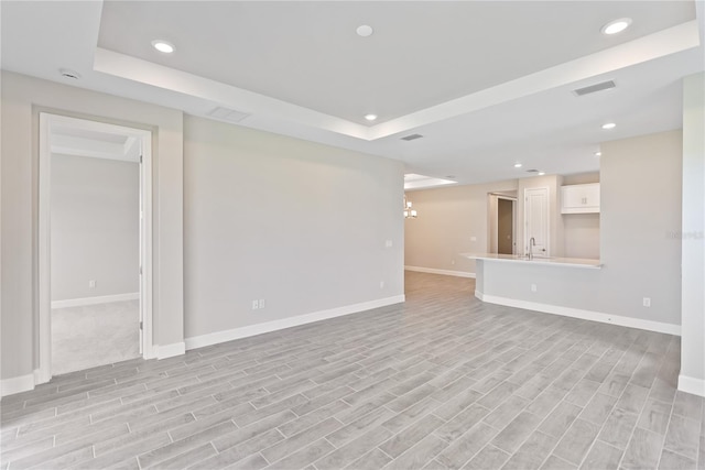 unfurnished room with a raised ceiling, an inviting chandelier, and light wood-type flooring