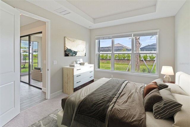 bedroom with a raised ceiling, light colored carpet, and access to outside