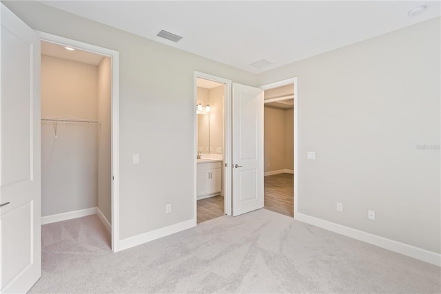 unfurnished bedroom featuring sink, a walk in closet, light carpet, ensuite bath, and a closet