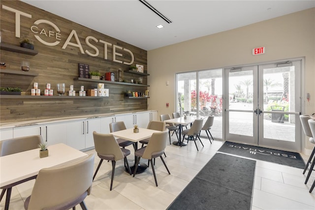 dining area with wood walls, french doors, and light tile flooring