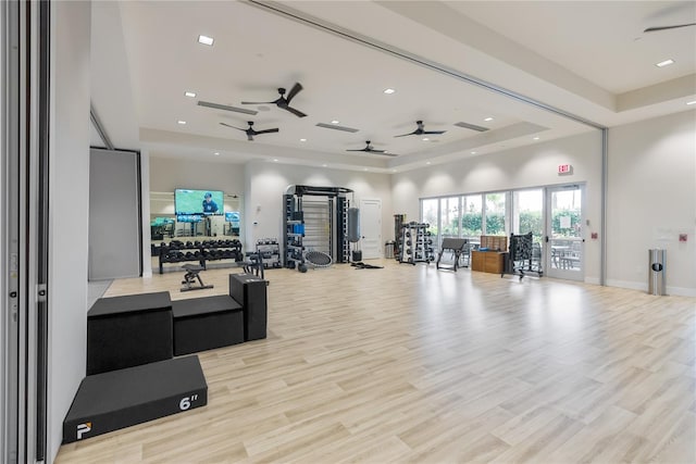 exercise room featuring a tray ceiling, ceiling fan, and light wood-type flooring