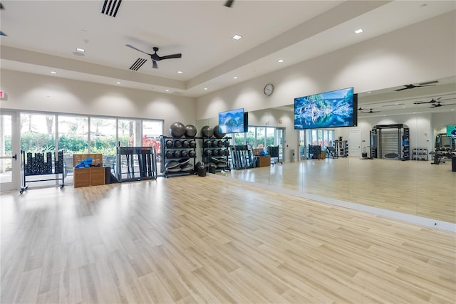 gym with light hardwood / wood-style floors, ceiling fan, and a towering ceiling