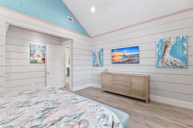 bedroom featuring light hardwood / wood-style floors, wood walls, and high vaulted ceiling