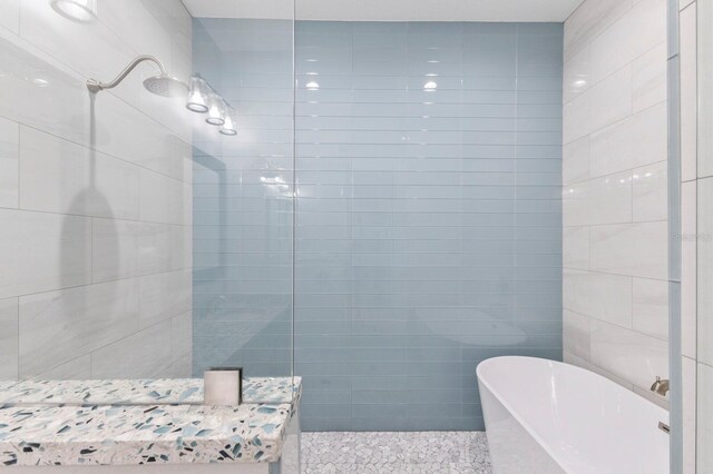 bathroom featuring shower with separate bathtub and tile walls