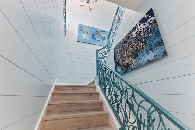 staircase with wooden walls and a chandelier