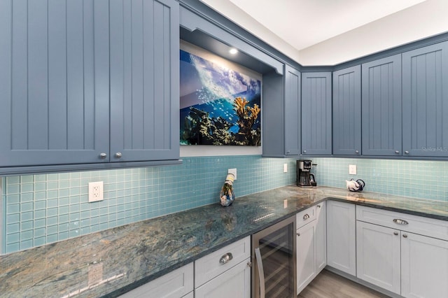 kitchen with dark stone countertops, wine cooler, white cabinets, backsplash, and light wood-type flooring