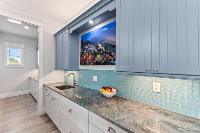 kitchen featuring light hardwood / wood-style floors, tasteful backsplash, sink, white cabinetry, and dark stone countertops