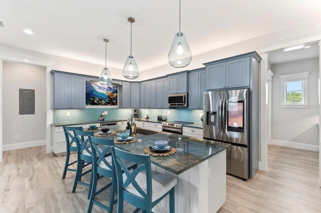 kitchen featuring tasteful backsplash, an island with sink, a kitchen breakfast bar, stainless steel appliances, and light hardwood / wood-style flooring